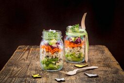 Springtime layered salad with rice, vegetables and daisies in jars