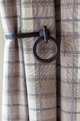 Cast-iron curtain holdback holding checked curtain in shades of beige