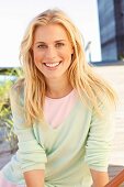 A young blonde woman on a beach wearing a pastel green jumper and a pink mini dress