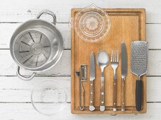 Kitchen utensils: a pot, a measuring jug, a citrus juicer, cutlery, a grater and a peeler
