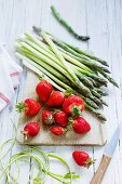 An arrangement of fresh strawberries and green asparagus on a wooden board