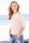 Dunkelblonde junge Frau in hellem Strickpulli und Jeans am Strand