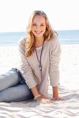 A young blonde woman on a beach wearing a long-sleeved beige shirt and jeans