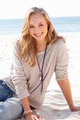 Junge blonde Frau in beigem Langarmshirt und Jeans am Strand