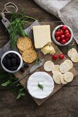 A cheese platter with sesame seed and wheat crackers, herbs, cherries and blackberries