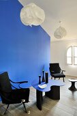 Schwarzer Armlehnstühle und blauer Designertisch vor gleichfarbigem Raumteiler