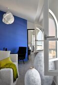Grosse, weiße Laternen vor Rundbogenfenster und Sofa im Wohnraum mit blauem Raumteiler