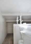 Space-saving fitted cupboards under sloping ceiling and artistic candlesticks in white bedroom