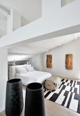 Weißes Schlafzimmer mit Baumrinden-Kunstobjekten, schwarzen Gefäßen und schwarz-weißem Teppich