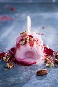 A melting strawberry ice cream on a stick, topped with chopped pecans