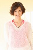 A brunette woman wearing a pink top and a transparent white knitted jumper