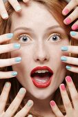 A red-haired woman surrounded by several hands wearing different coloured nail varnishes