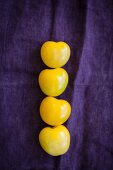 Four yellow tomatoes on a violet cloth