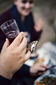 A butterfly on a hand holding a glass of red wine