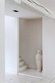 Schlichter weißer Treppenaufgang hinter Wandscheibe und Bodenvase