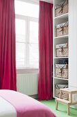 Red curtains and storage baskets on white shelves in bedroom