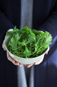 A person holding a bowl of fresh rapini