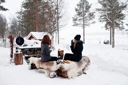 Two women sitting in snowy landscape next to fire having winter picnic