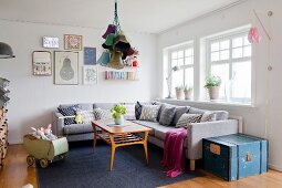 Grey couch, collection of scatter cushions and vintage dolls' pram in cosy living room with retro ambiance