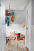 Wooden ceiling and foot of staircase in white, wood-clad, Scandinavian hallway with retro ambiance