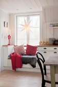 Fur blanket and cushions on window seat below star decoration in kitchen window