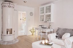 Desk below wall-mounted cabinet and armchair next to Swedish tiled stove