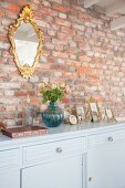 Gilt-framed mirror on rustic brick wall above family photos on pale blue sideboard