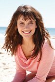 A brunette woman in a pink long-sleeved top on the beach