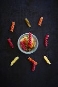Colourful fusilli in a glass and scattered next to the glass