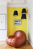 Lounge-Ledersessel vor gelber Wand und schwarzen Lampenschirmen in restaurierter Altbauwohnung