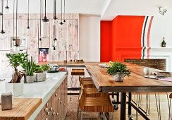 Island counter with white worksurface, pendant lamps made from jars, long dining table and bar stools in open interior