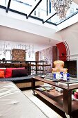 Sofas and armchair around coffee table in living area below gallery and glass roof