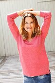 A woman with dark blonde hair wearing a pink knitted jumper and jeans