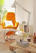 Orange armchair with footstool and standard lamp in front of low coffee table on castors