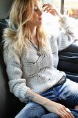 Junge blonde Frau in weißem Strickpullover und Jeans sitzt auf der Rückbank im Auto