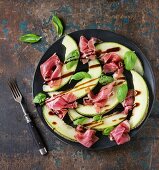 Sliced melon with ham and basil leaves, served on black ceramic plate