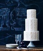 Weisser, mehrstöckiger Hochzeitstorte mit Zopfmuster vor blauer Hintergrund