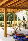 Wooden deckchair, pallet table and floor cushions on roofed terrace