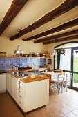 Terrace doors next to dining area in country-house kitchen below renovated wood-beamed ceiling