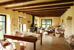 View past dining table into open-plan living area with fireplace and wood-beamed ceiling in renovated country house