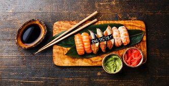Nigiri Sushi Set on bamboo green leaf on olive wood board with soy sauce on wooden background
