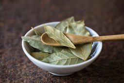 Dried bay leaves with a wooden spoon in a bowl
