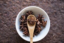 Star anise with a wooden spoon in a bowl (seen from above)