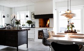 Dining area, fire in open fireplace and island counter made from old workbench in open-plan kitchen