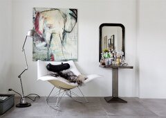 Designer-Schaukelstuhl mit Tierfell vor Bild mit Elefantenmotiv, Stehlampe im Industriestil und Minibar