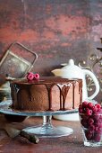 A chocolate cake with chocolate glaze and raspberries on a cake stand