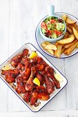 Barbecued chicken drumsticks and wings with potato wedges and salad