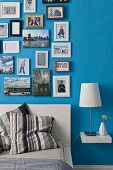 Verschiedene gerahmte Fotos und Botschaften in 'Petersburger Hängung' an blauer Wand über Betthaupt