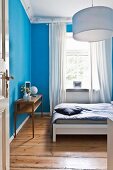 Bedroom with bright blue walls and board floor in restored period apartment