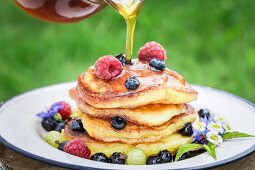 Maple syrup being drizzled onto a pile of pancakes with fresh berries